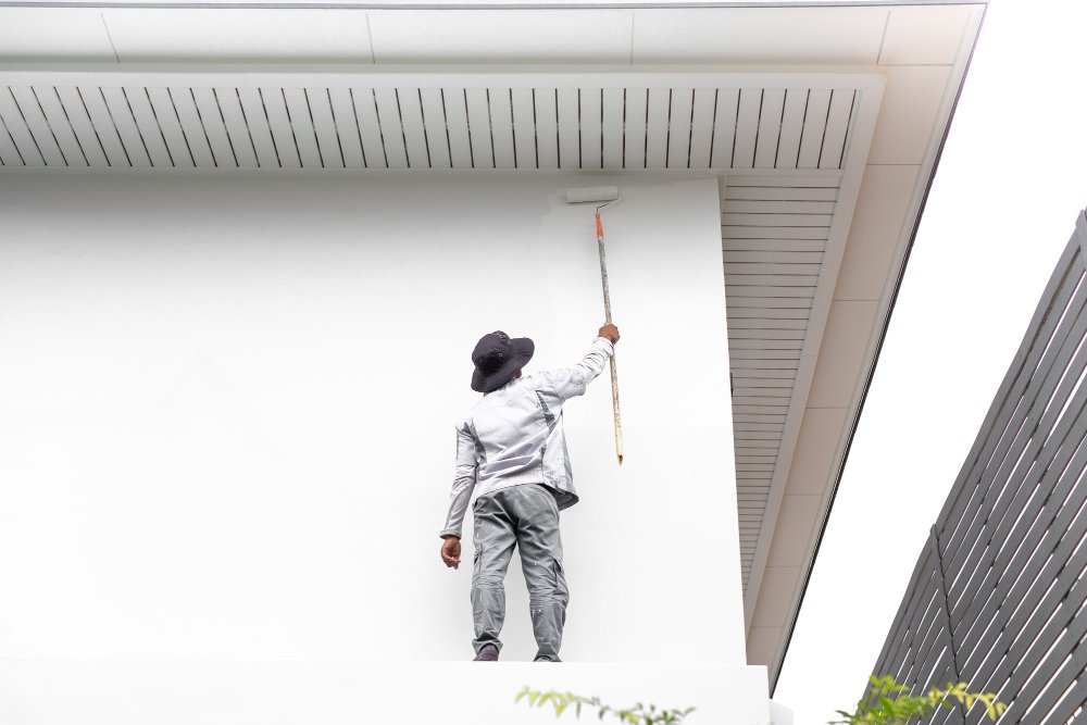 Painter use paint roller on white wall outside isolated in white background